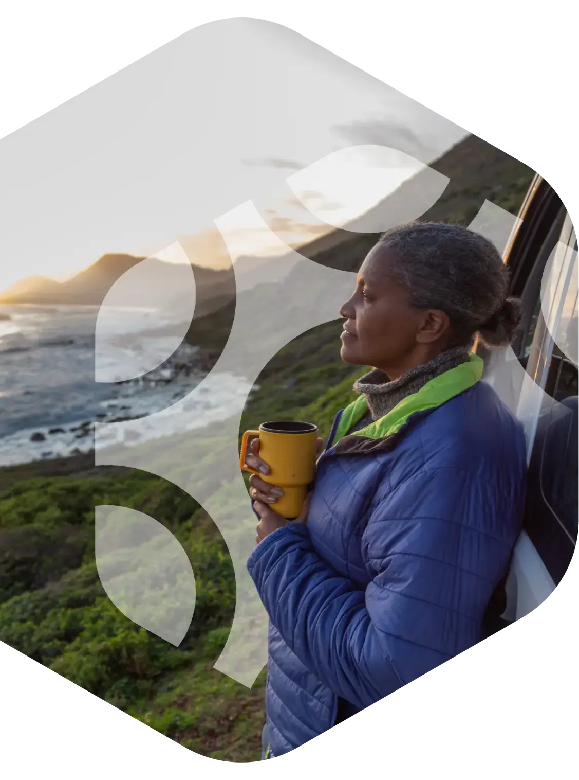 On the left, a mature black woman with grey hair is pictured in a profile view, wearing a blue jacket and holding a yellow mug while looking out over a scenic, misty coastline. The image is framed within a large, red-bordered hexagonal shape.